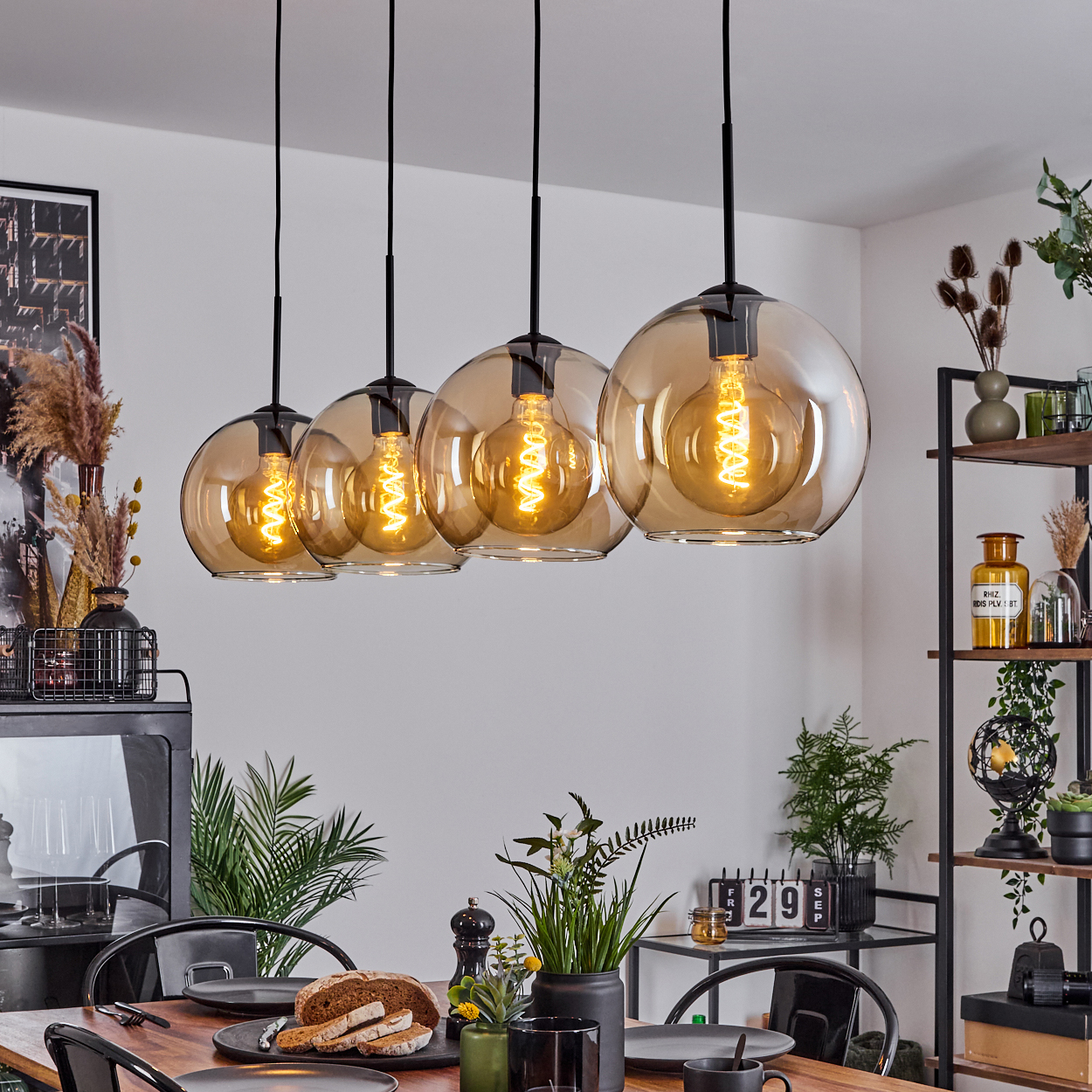 Esszimmer mit Pendelleuchten, Tisch mit Gläsern und Brot gedeckt und Dekorationsartikeln auf Regalen.