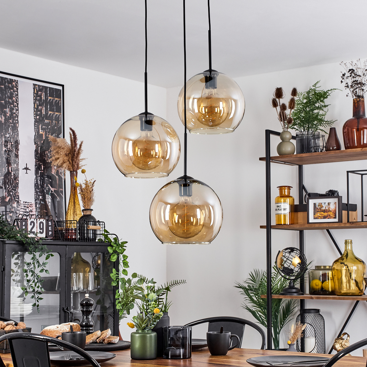 Ein Esszimmer mit drei Hängelampen mit bernsteinfarbenen Glühbirnen und Dekorationsartikeln.