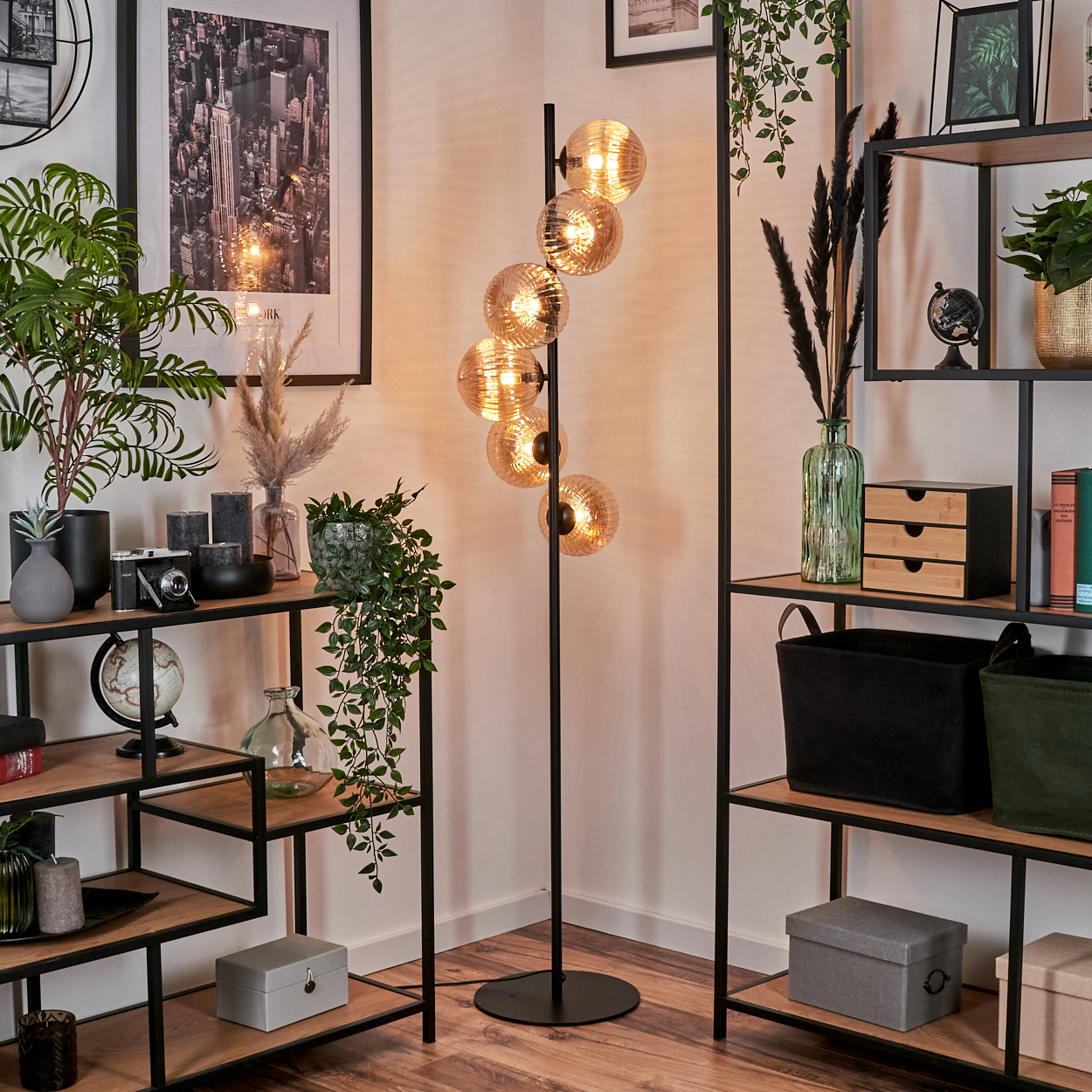Beleuchtete Stehlampe mit bernsteinfarbenen Glaskugeln, vor Dekoration und Regalen mit Gegenständen.