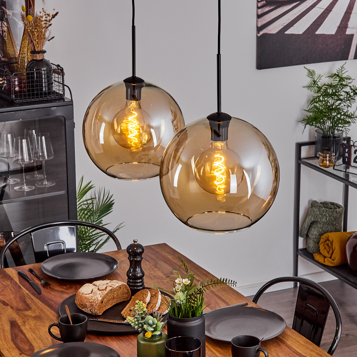 Zwei Pendelleuchten mit orangefarbenen Glühbirnen, die über einem Holztisch hängen, der mit Tellern und Essen in einem Esszimmer gedeckt ist.