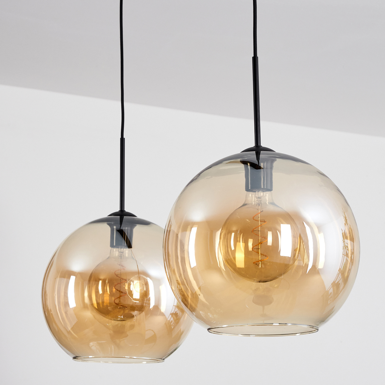 Zwei Pendelleuchten mit bernsteinfarbenen Glaskugeln und sichtbaren Glühbirnen, die von der Decke hängen.