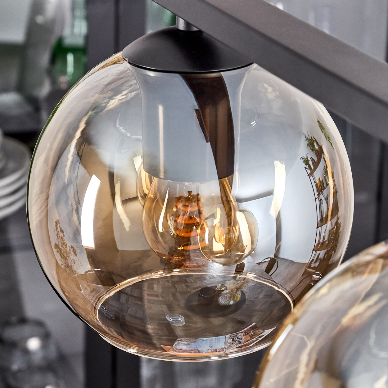 Nahaufnahme einer bernsteinfarbenen Glaskugel mit sichtbarer Glühbirne. Schwarzer Metallrahmen.