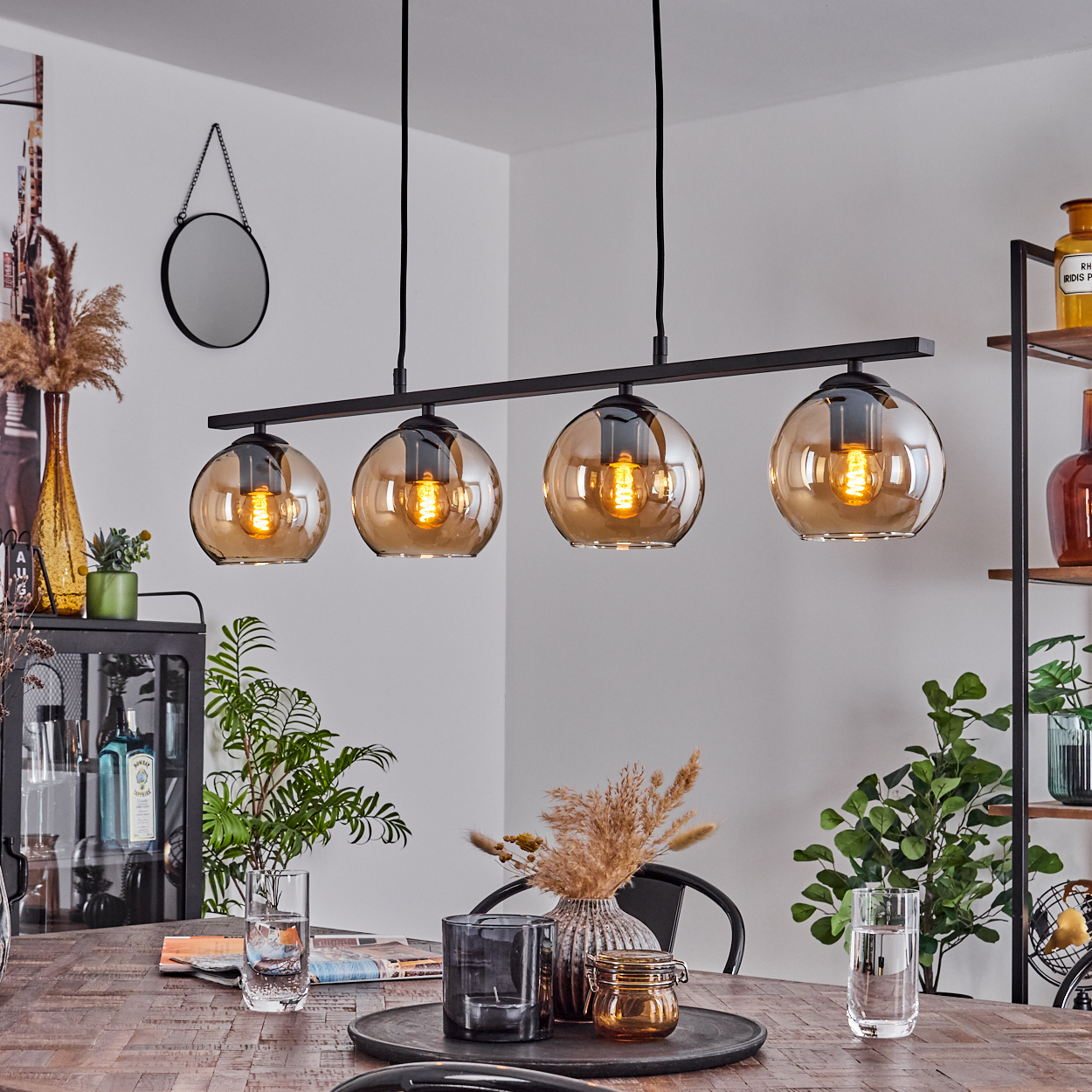 Ein Esszimmer mit einer bernsteinfarbenen Pendelleuchte über einem Holztisch, Pflanzen und anderen Dekorationen.