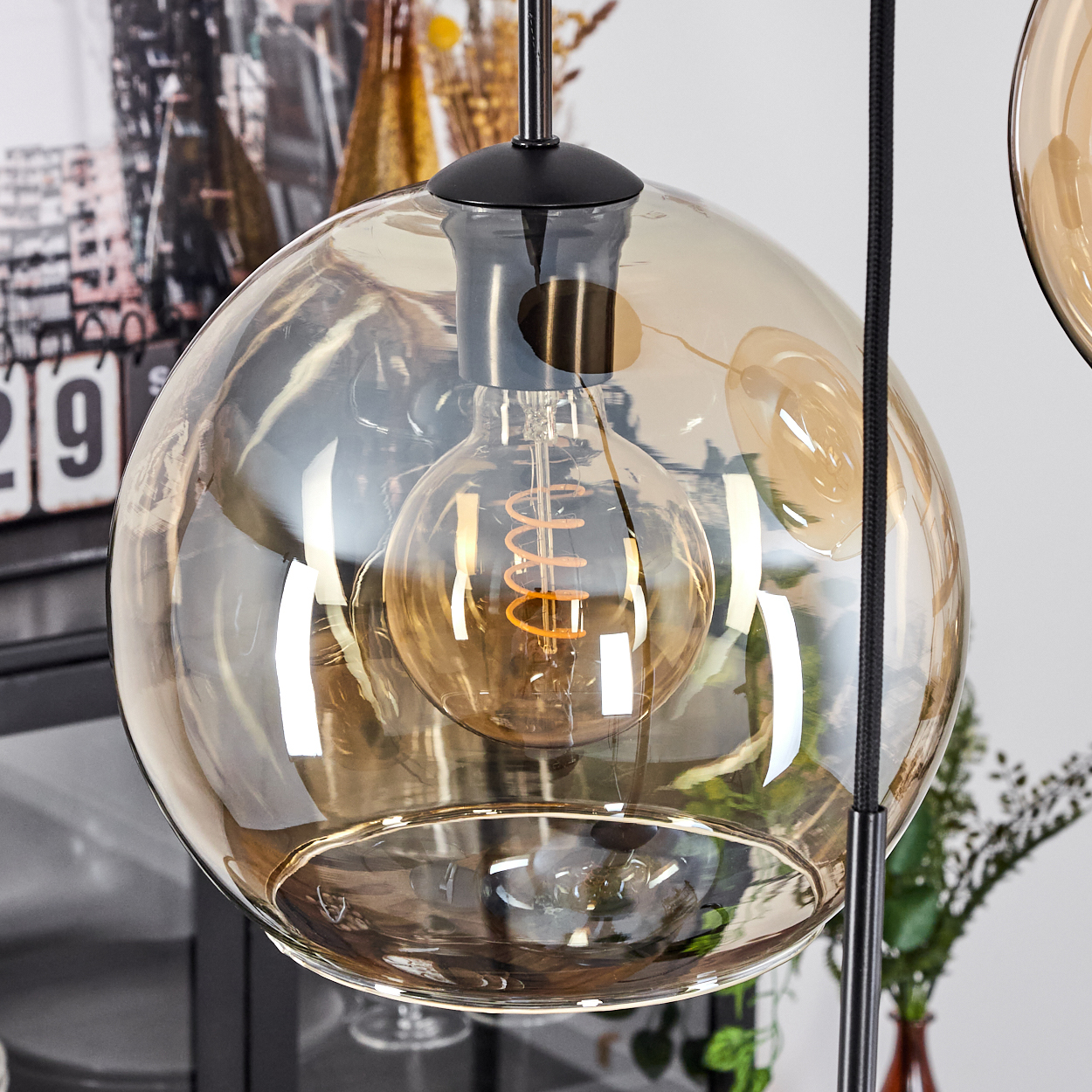 Nahaufnahme einer bernsteinfarbenen Glaskugelleuchte mit beleuchteter Edison-Glühbirne; schwarzer Rahmen.