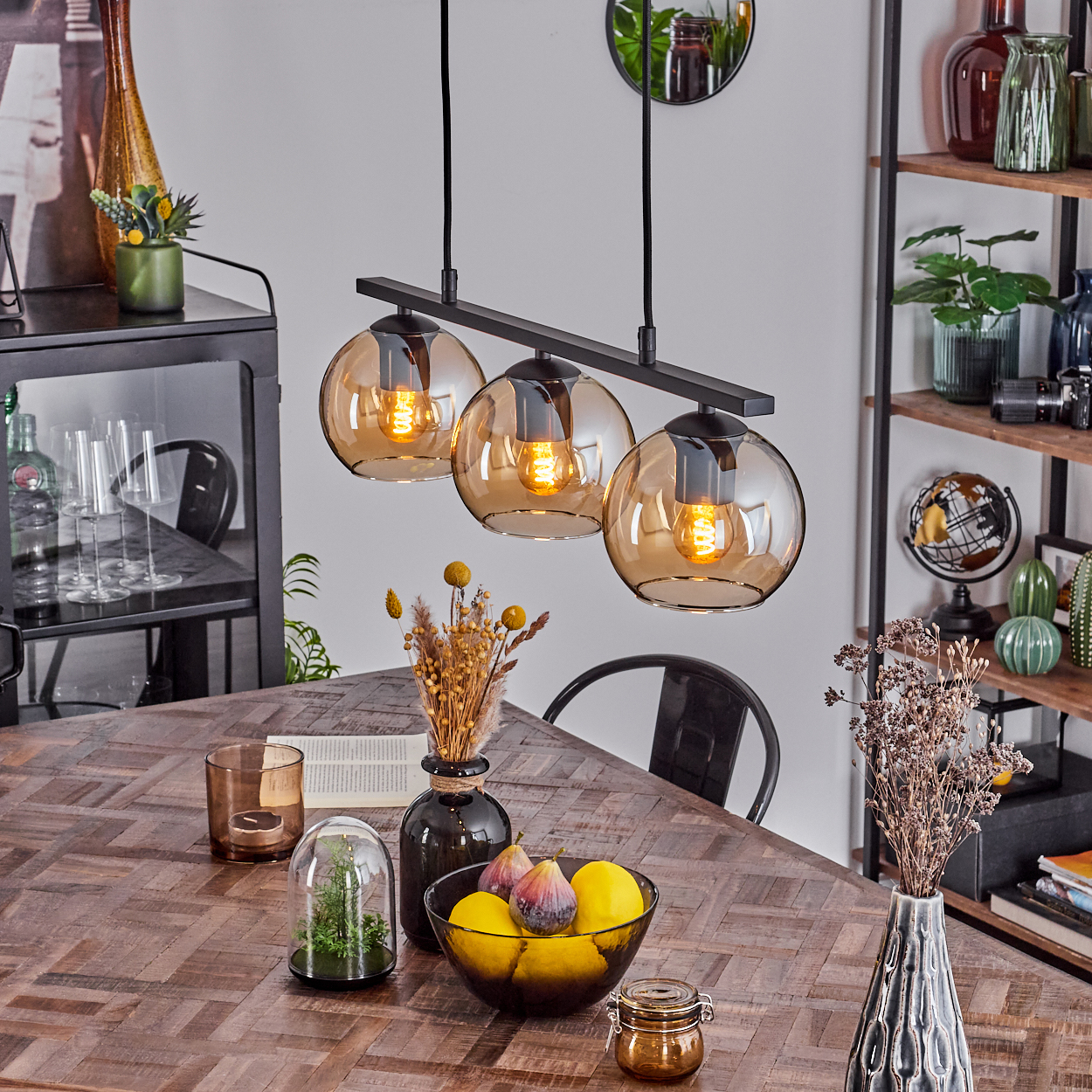 Esszimmer-Setup mit drei bernsteinfarbenen Glaskugelleuchten. Tisch mit Deko, Obst und Blumen.