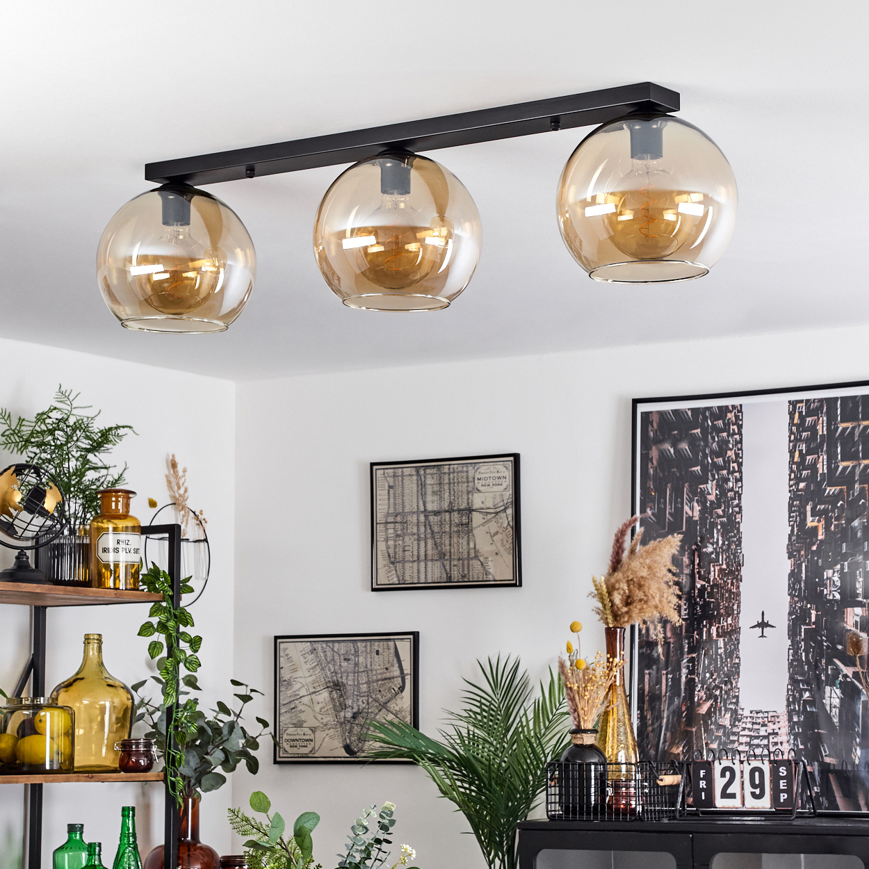 Deckenleuchte mit drei bernsteinfarbenen Kugeln in einem Esszimmer. Schwarze Halterung, weiße Decke.