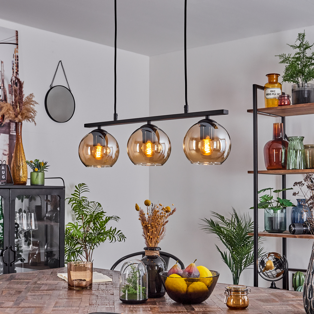 Esszimmer mit Holztisch, schwarzer Lampe mit Bernsteinkugeln und verschiedenen Dekorationsartikeln.