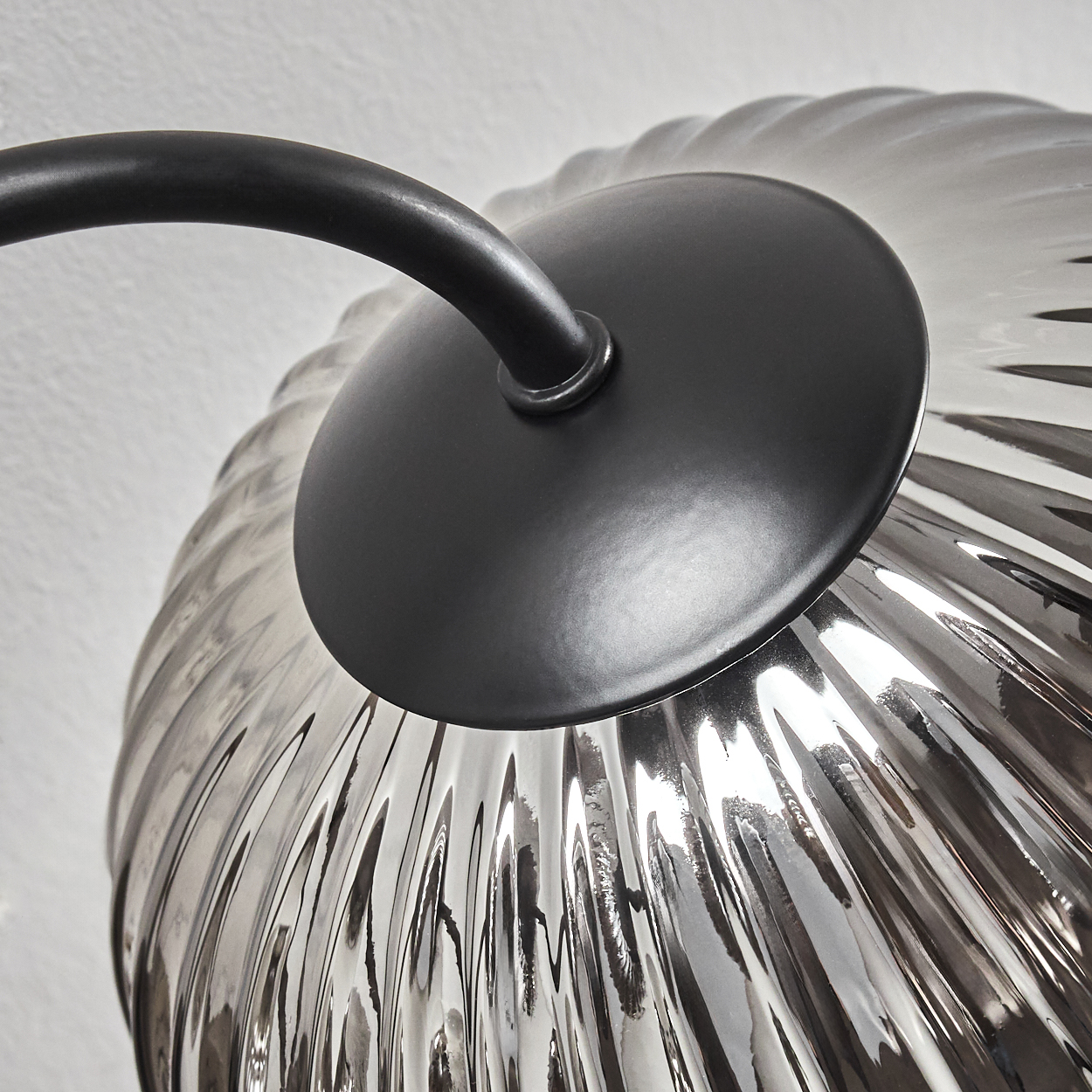 Nahaufnahme einer Metallleuchte mit geriffelten Glasschirmen, schwarzer Hintergrund.