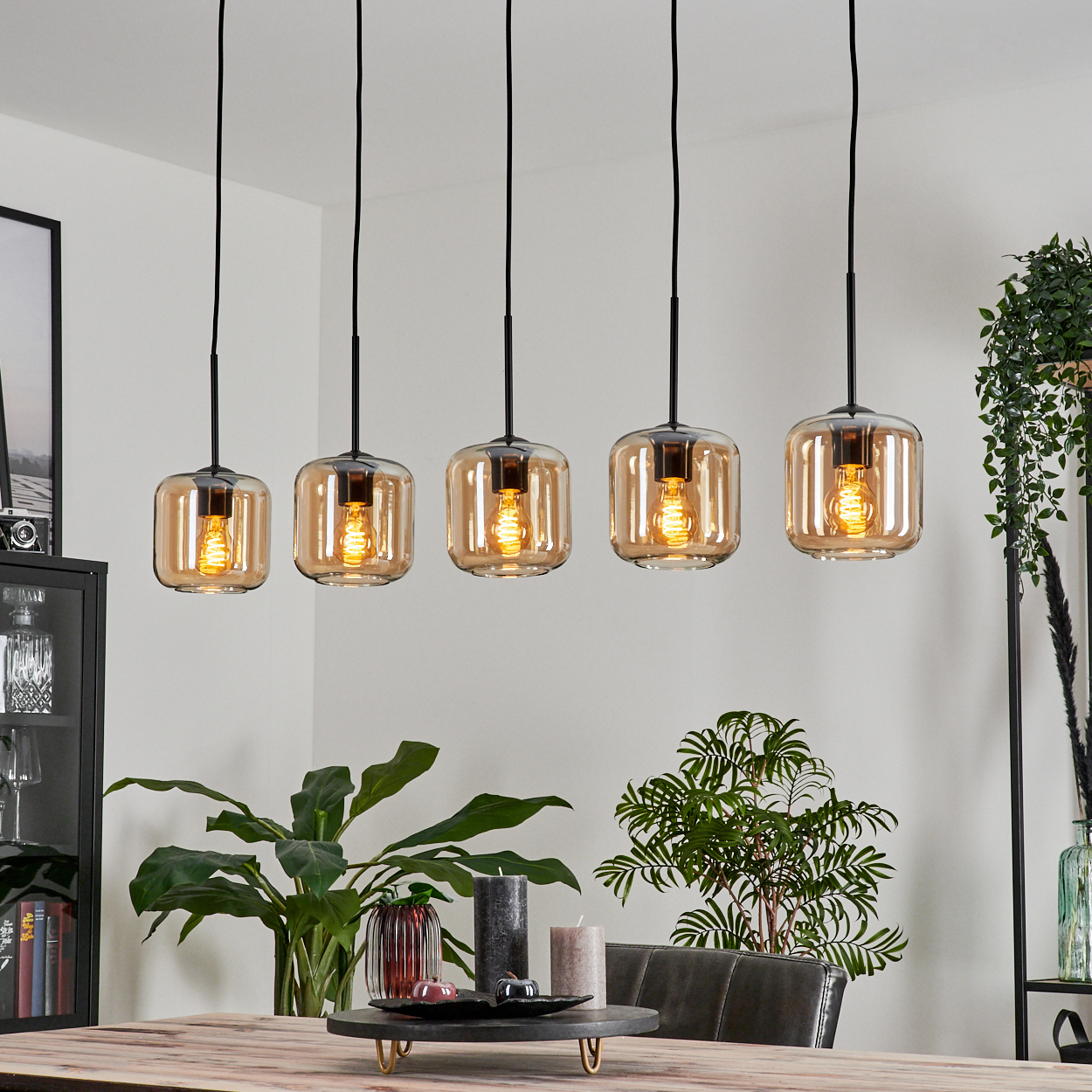 Esszimmer mit Holztisch und fünf Pendelleuchten mit bernsteinfarbenen Glasschirmen.
