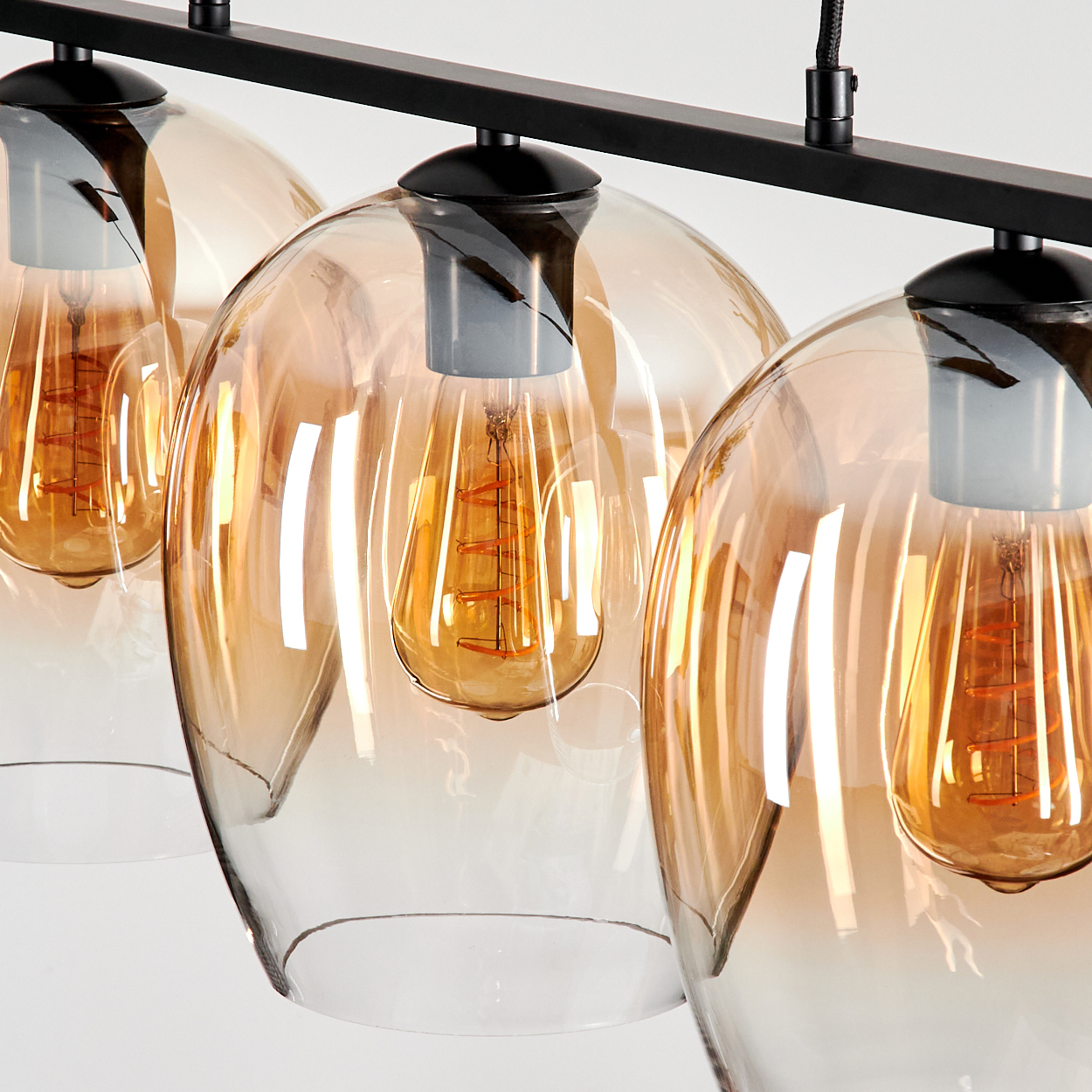 Drei Pendelleuchten mit bernsteinfarbenen Glasschirmen und Edison-Glühbirnen, schwarze Halterung, weißer Hintergrund.