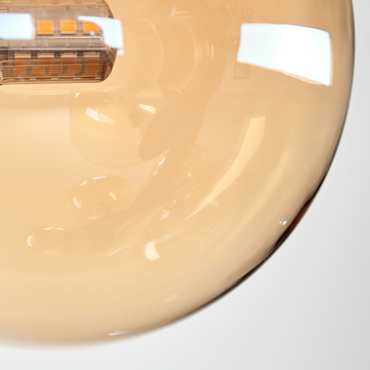 Nahaufnahme eines bernsteinfarbenen Glasschirms mit weißem Hintergrund und einer LED-Leuchte im Inneren.