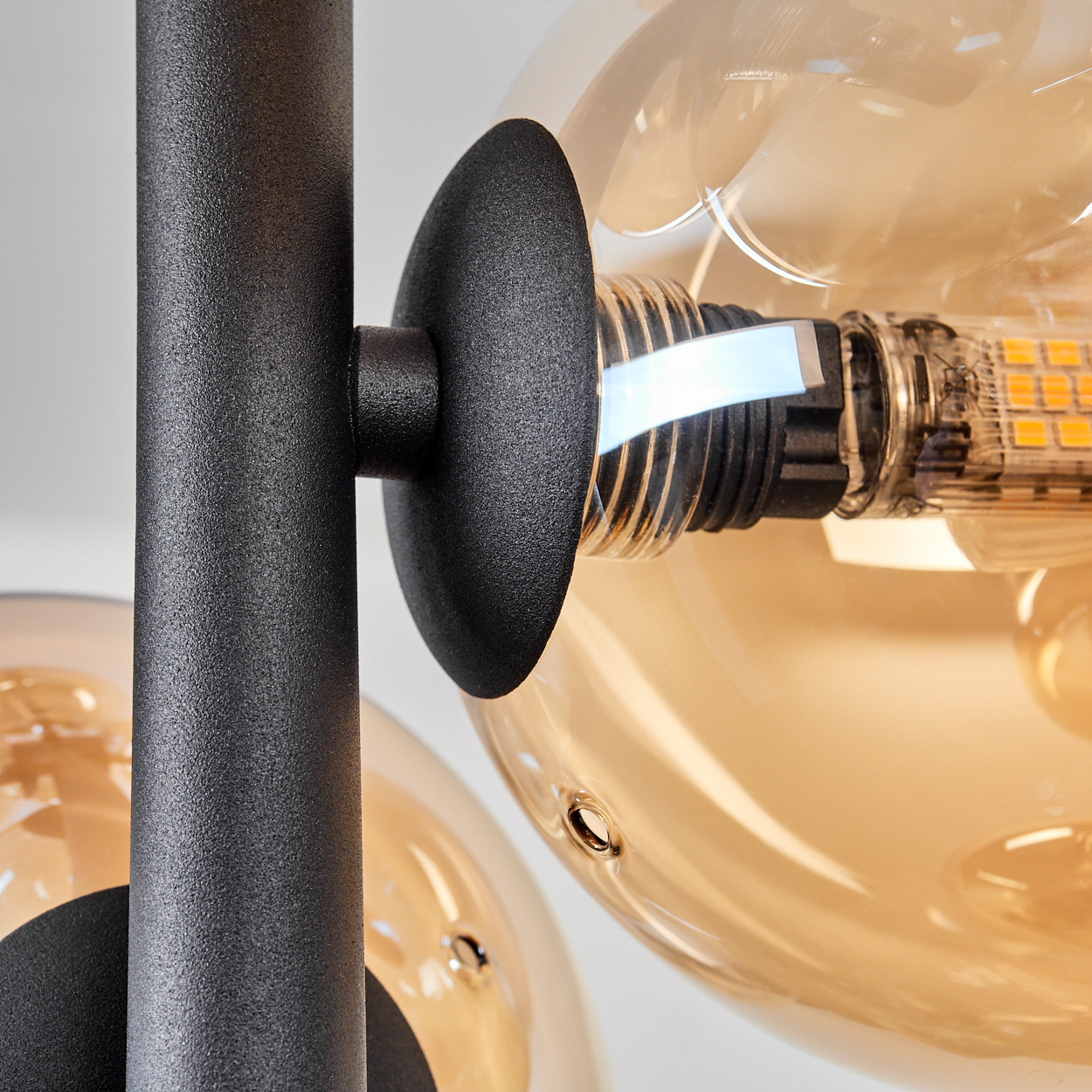 Detailaufnahme einer Hängelampe. Sie zeigt die Verbindung der Lampe und des bernsteinfarbenen Glasschirms.