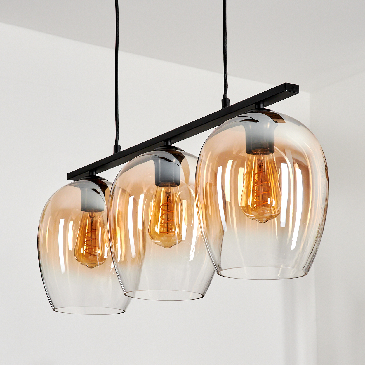 Nahaufnahme einer Pendelleuchte mit drei bernsteinfarbenen Glasschirmen und Edison-Glühbirnen.