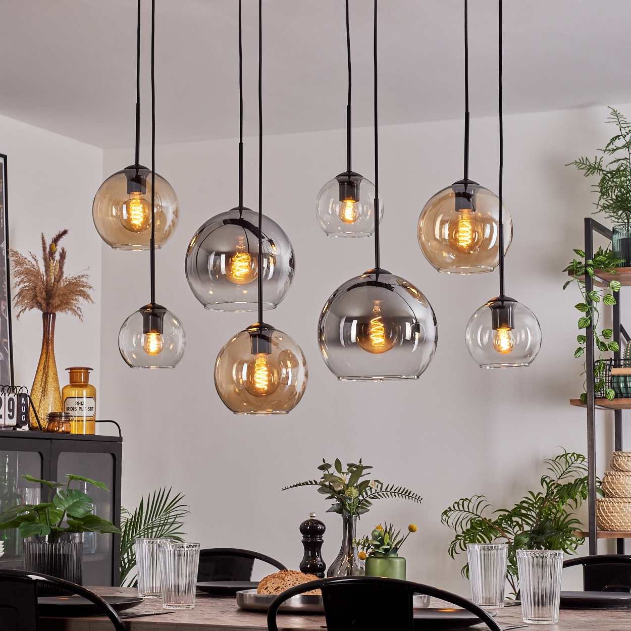 Ein Esszimmer mit acht Pendelleuchten mit bernsteinfarbenen und silbernen Glaskugeln über einem Holztisch.