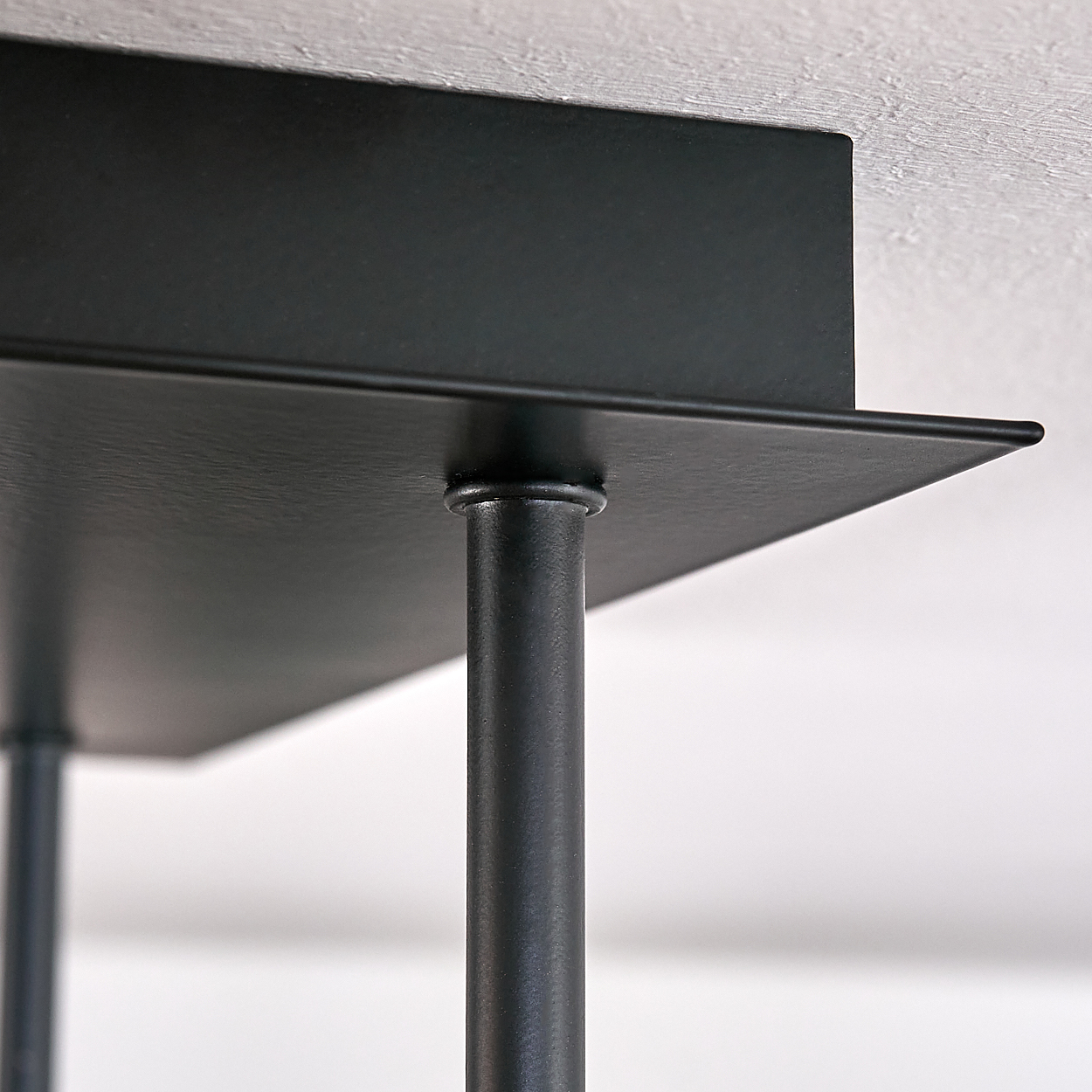 Eine schwarze Deckenleuchte. Die Leuchte hat einen quadratischen Sockel und Stäbe für die Lichter.