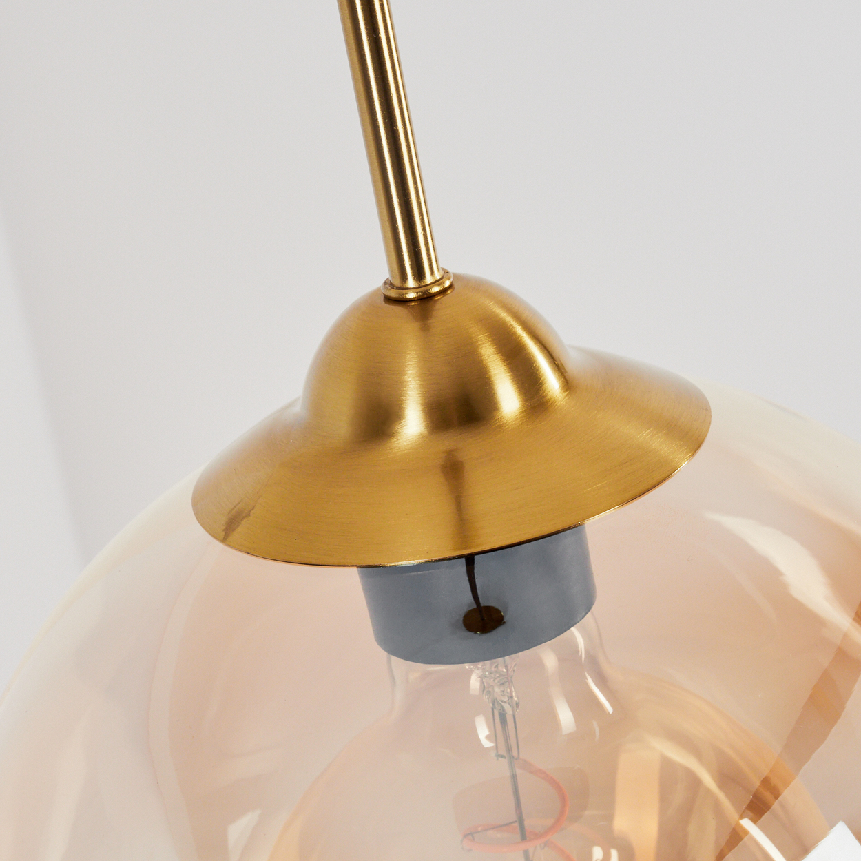 Nahaufnahme einer Pendelleuchte. Bernsteinfarbener Glaskugel, goldfarbener Glühbirnenhalter und graue Basis.