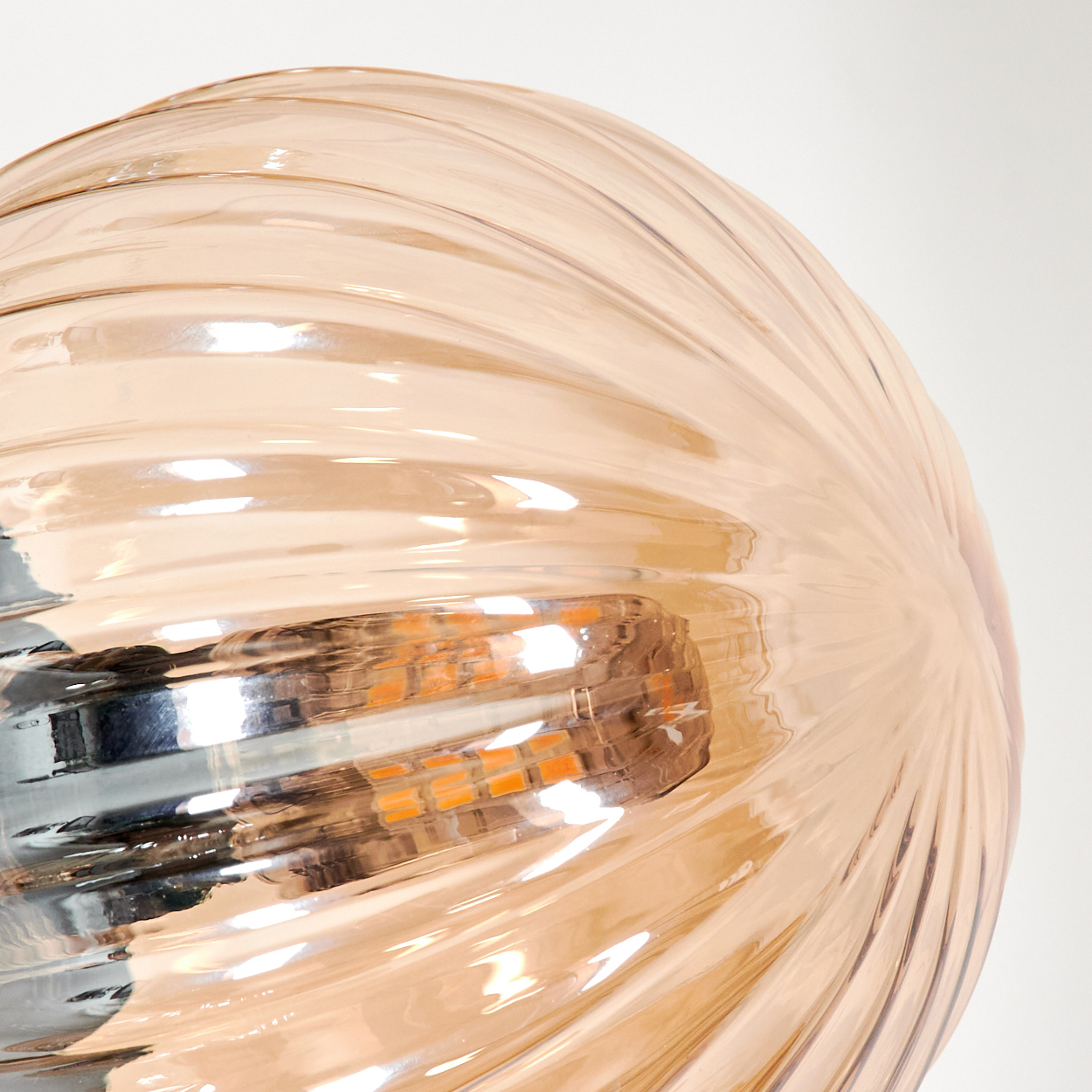 Nahaufnahme einer bernsteinfarbenen Glaskugel mit Spiraldesign. Eine Glühbirne ist sichtbar.