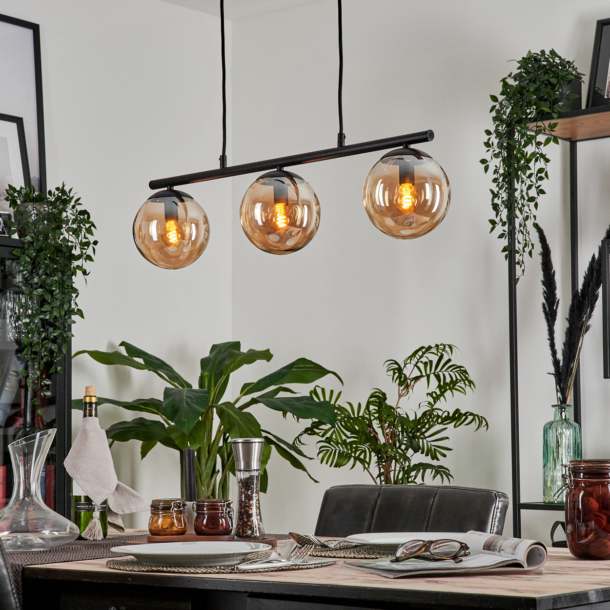 Esszimmer mit Tisch, drei Lampen mit Bernsteinschirmen, Pflanzen und Dekorationen.