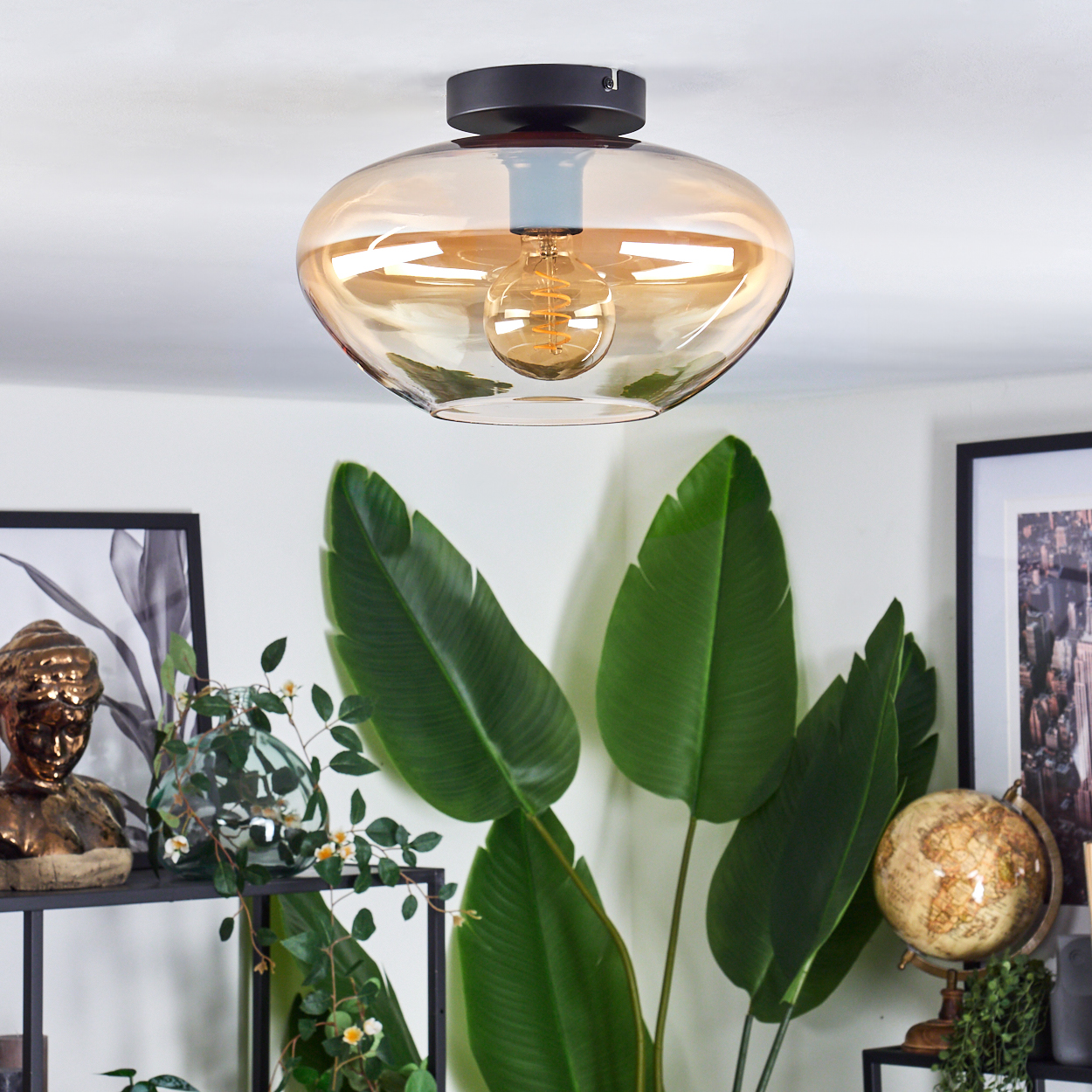Deckenlampe mit bernsteinfarbenem Glasschirm, schwarzem Sockel und Dekoelementen im Raum.