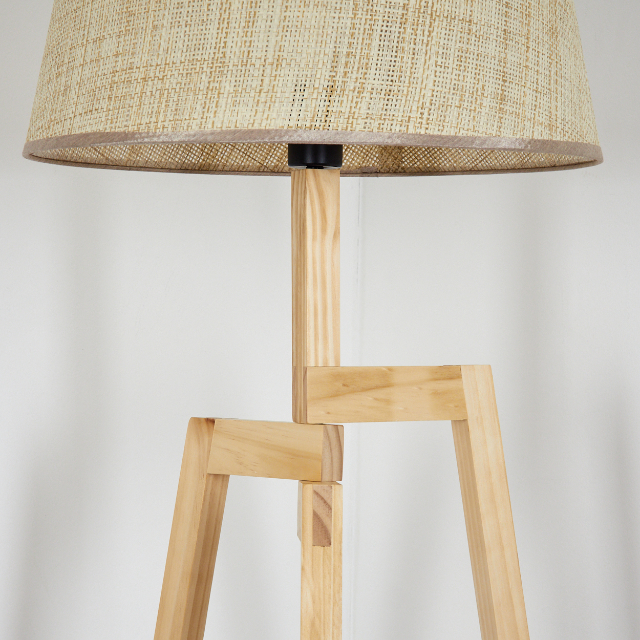 Holz-Stehlampe mit beigem Schirm und Holzrahmen, vor einer weißen Wand.