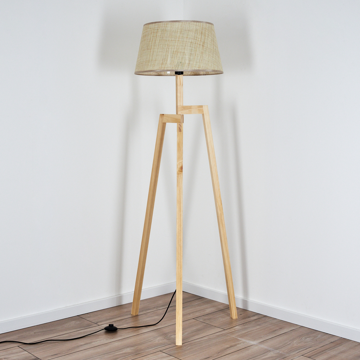 Holz-Stativ-Stehlampe mit beigem Lampenschirm, in einer weißen Ecke platziert.