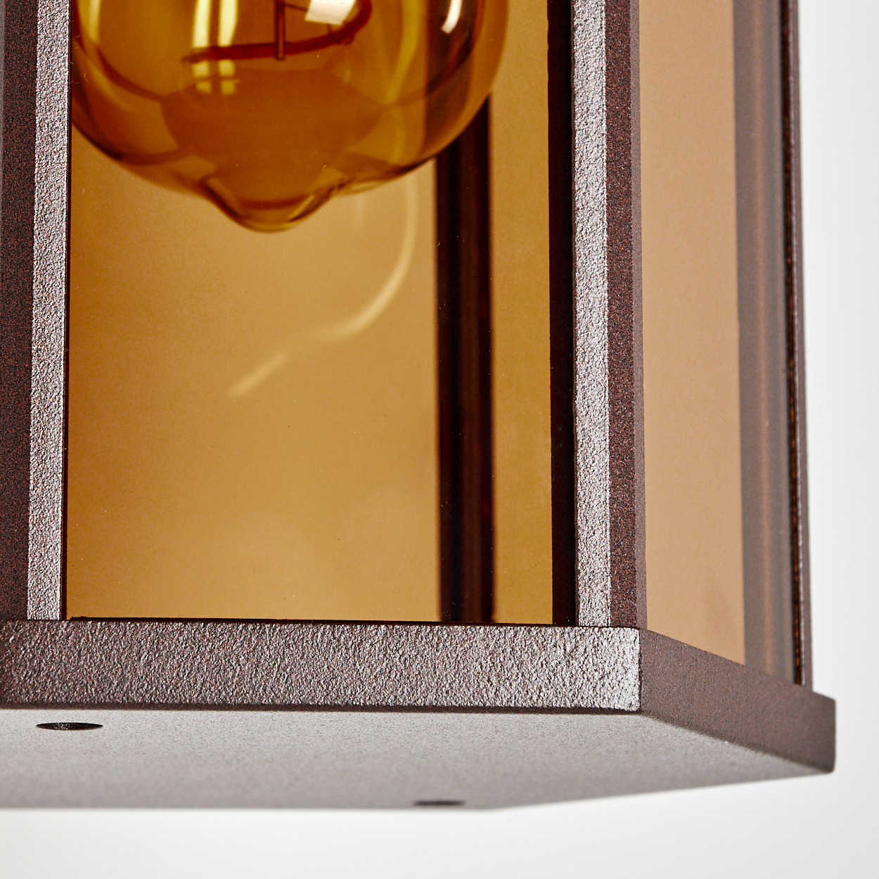 Nahaufnahme einer Bronze-Wandlampe mit bernsteinfarbenem Glas und sichtbarer Glühbirne.
