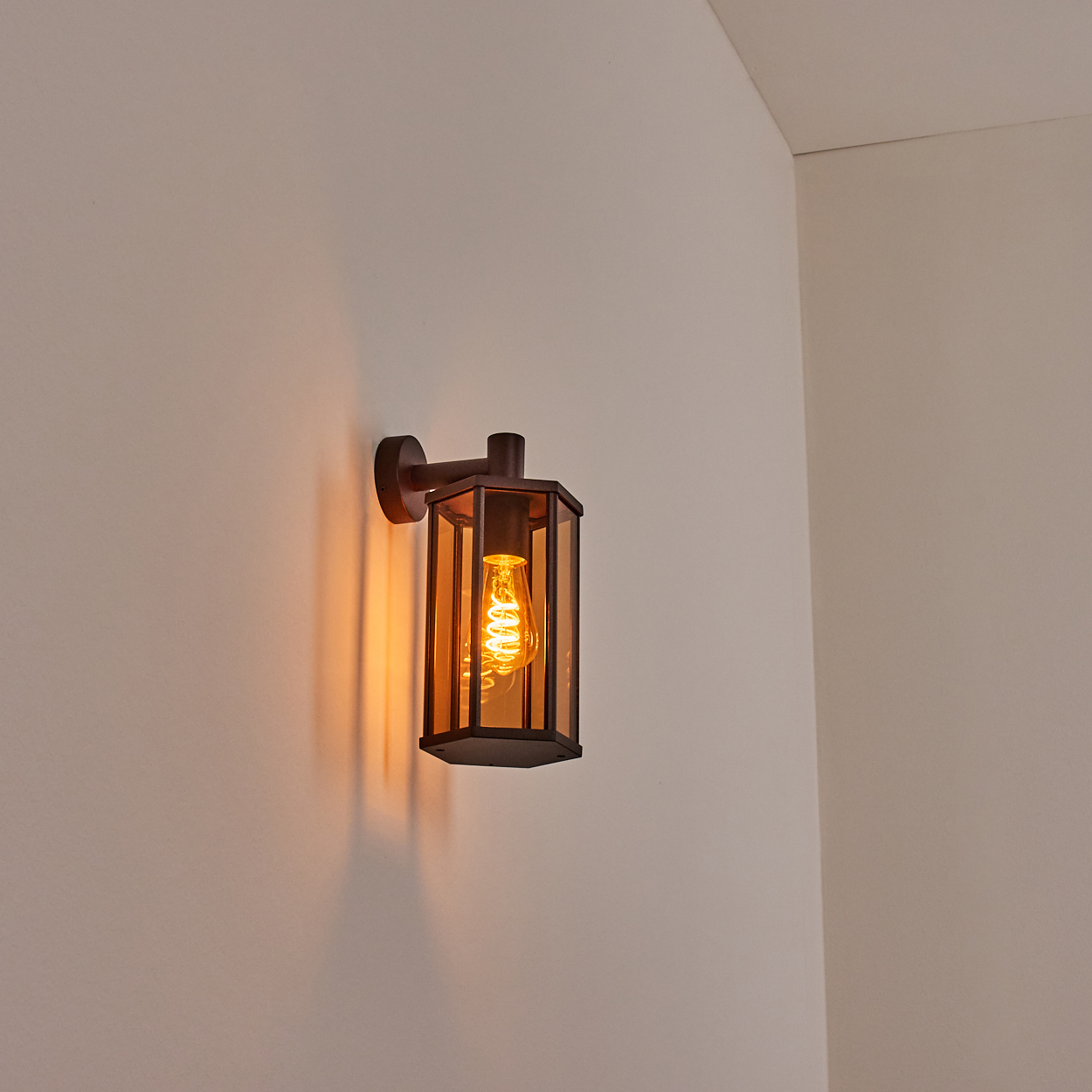 Eine bronzefarbene Wandleuchte mit einem bernsteinfarbenen Glaspaneel und einer sichtbaren Glühbirne an einer Wand.