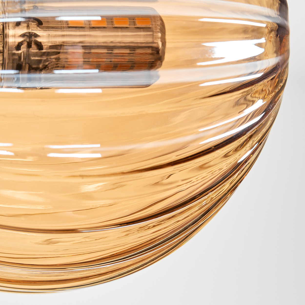 Nahaufnahme eines geriffelten bernsteinfarbenen Glasschirms mit brennender Glühbirne, zeigt Lichtbrechung.