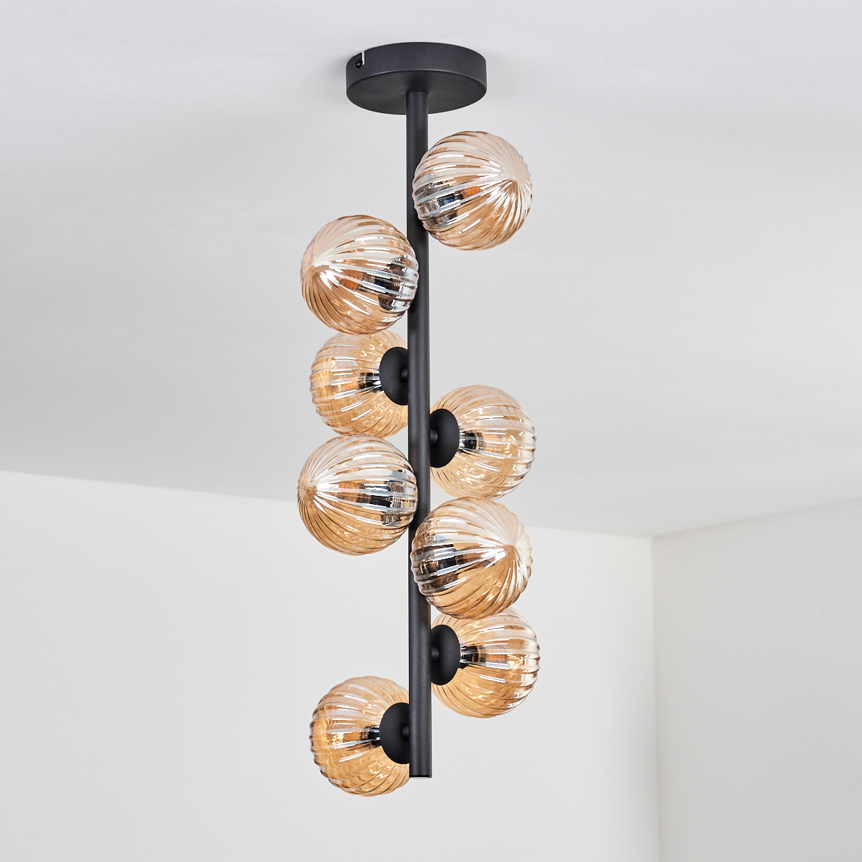 Eine vertikale Leuchte mit mehreren orangefarbenen Glaskugeln und einem schwarzen Metallrahmen.