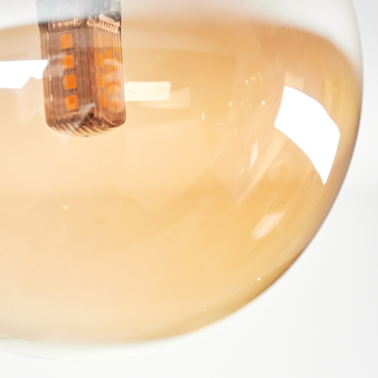 Nahaufnahme eines orangefarbenen Glaskugels mit einer Glühbirne im Inneren, weißer Hintergrund.