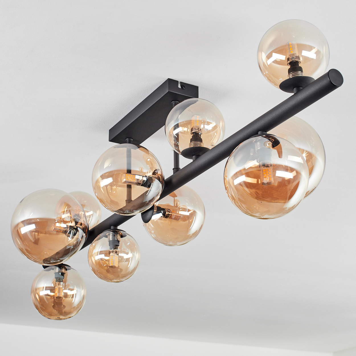 Eine Deckenleuchte mit mehreren orangefarbenen Glaskugeln und einem schwarzen Metallrahmen, weiße Decke.