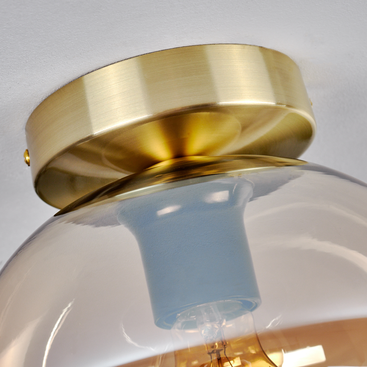 Nahaufnahme der Deckenleuchte. Ein goldfarbener Sockel und eine bernsteinfarbene Glaskugel mit einer sichtbaren Glühbirne.