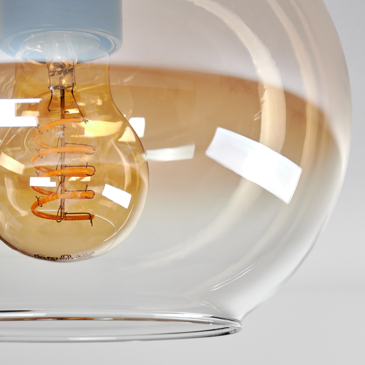 Nahaufnahme einer bernsteinfarbenen Glas-Pendelleuchte. Die Glühbirne mit dem Wendel ist sichtbar.