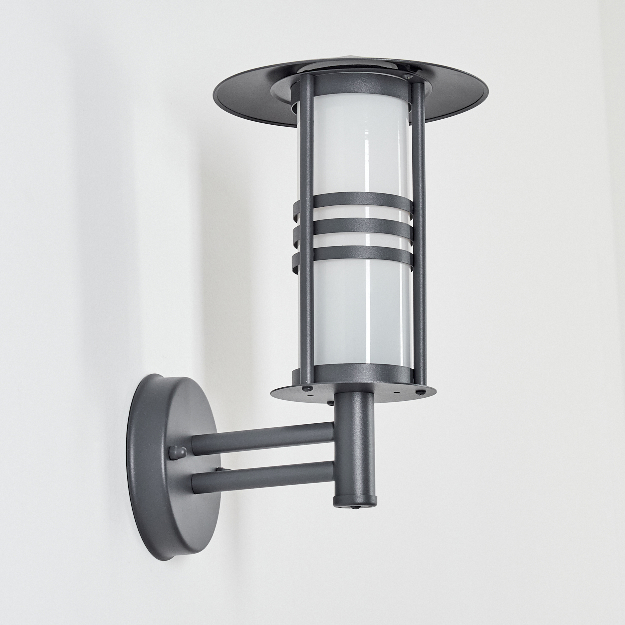 Graue Außenwandleuchte. Zylindrischer Lichtdiffusor, konischer Schirm. Auf weißem Hintergrund montiert.