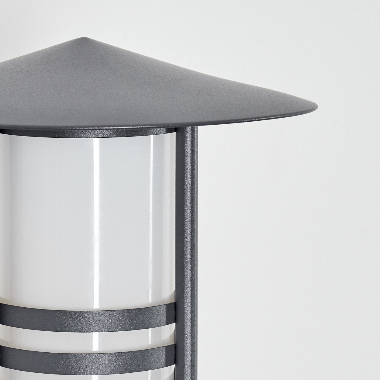 Eine graue Außenlampe, zylindrisch, mit einem weißen Innenlicht, an einer Wand montiert.