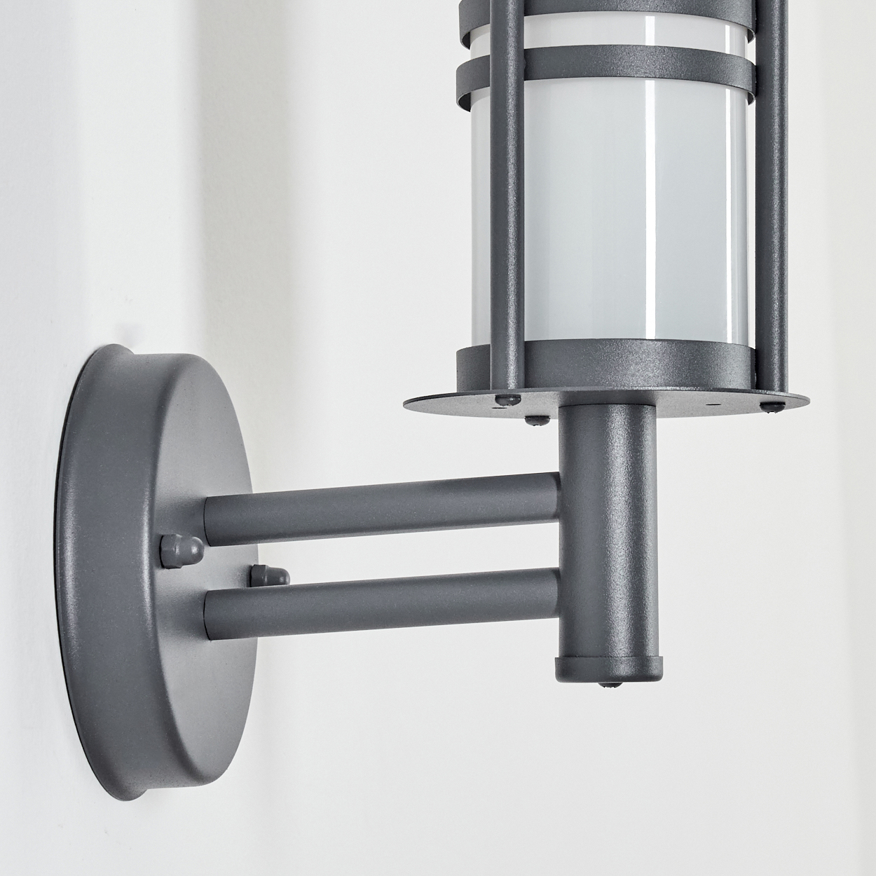 Eine Wandleuchte für den Außenbereich mit grauer Metalloberfläche, zylindrischer Glasabdeckung und gebogenem Arm.