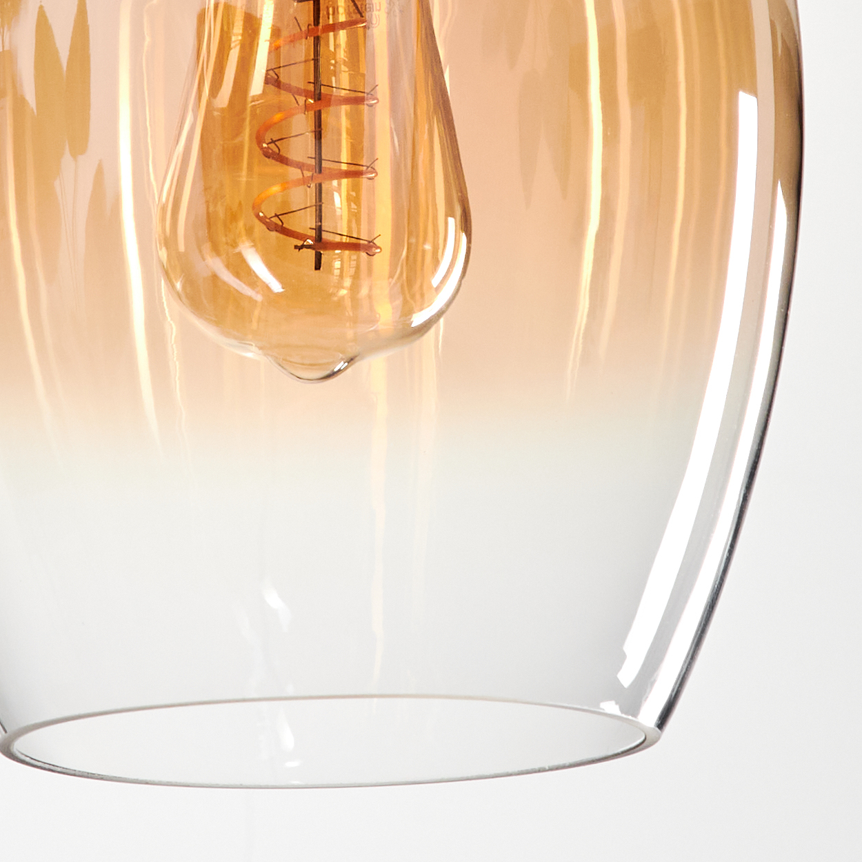 Nahaufnahme einer Glühbirne in einer bernsteinfarbenen Glas-Pendelleuchte, wobei das Glas einen Gradienteneffekt aufweist.
