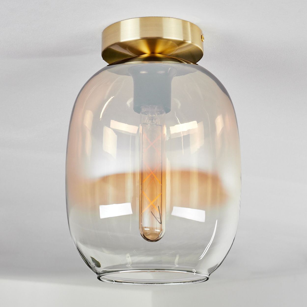 Eine Glashängelampe mit goldenem Sockel und bernsteinfarbenem Schirm, mit sichtbarer Glühbirne.