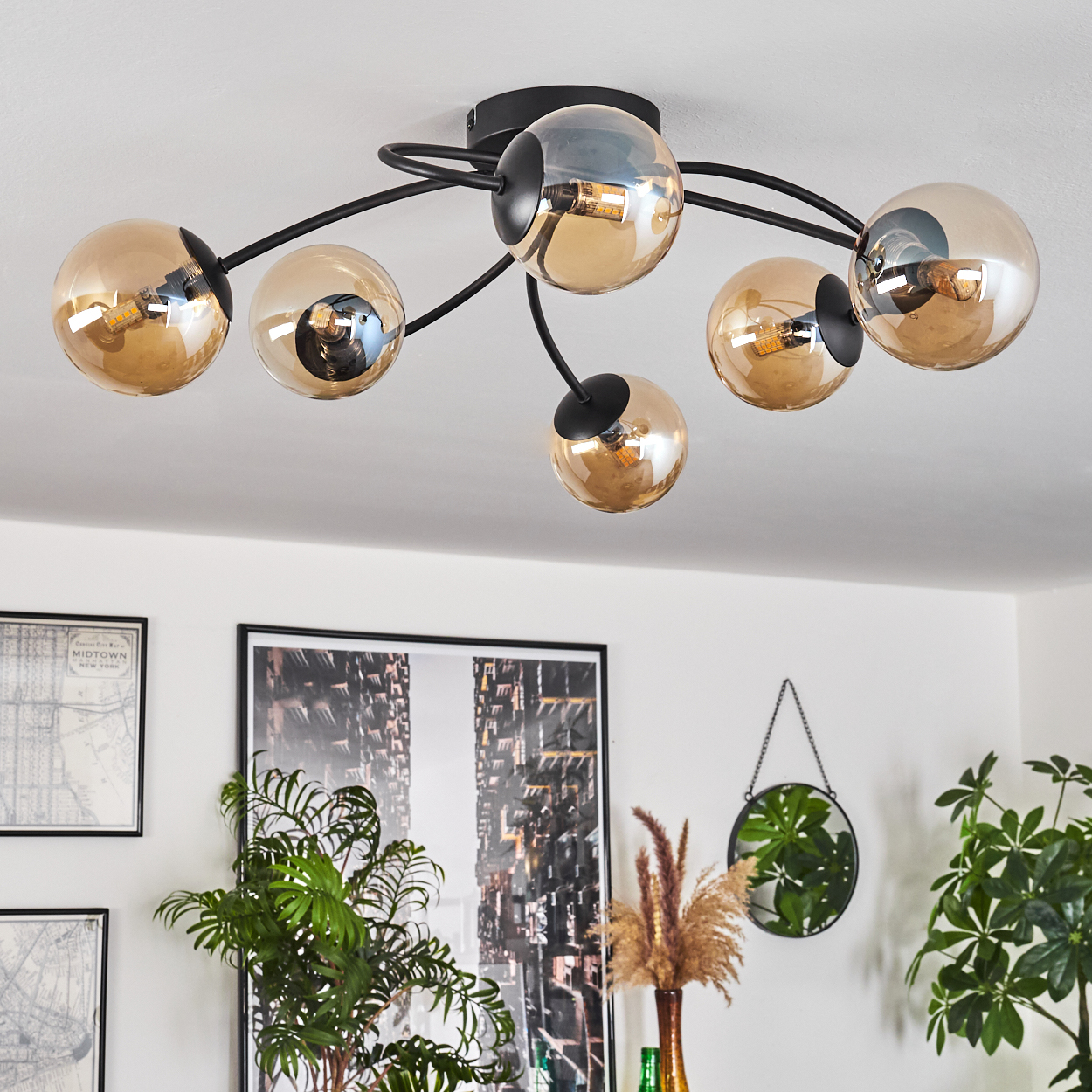 Eine Deckenlampe mit sechs bernsteinfarbenen Glaskugeln. Der Hintergrund umfasst Pflanzen, Kunstwerke und einen Spiegel.