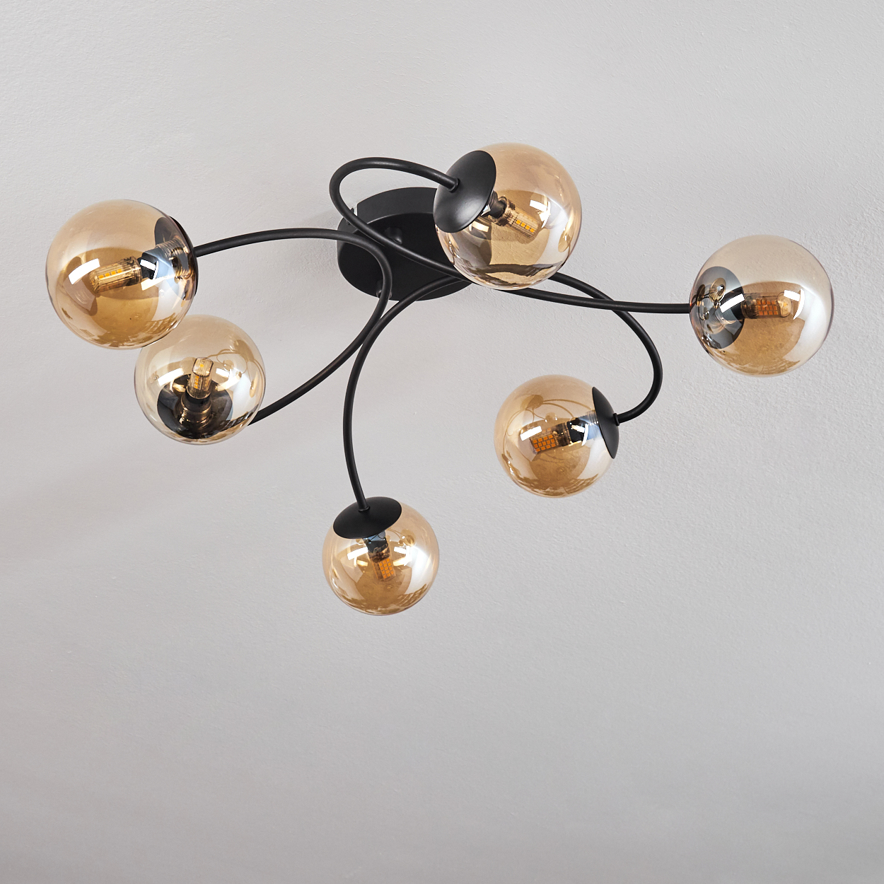 Deckenlampe mit sechs bernsteinfarbenen Glaskugeln. Jede Kugel hat eine Glühbirne. Weiße Decke.