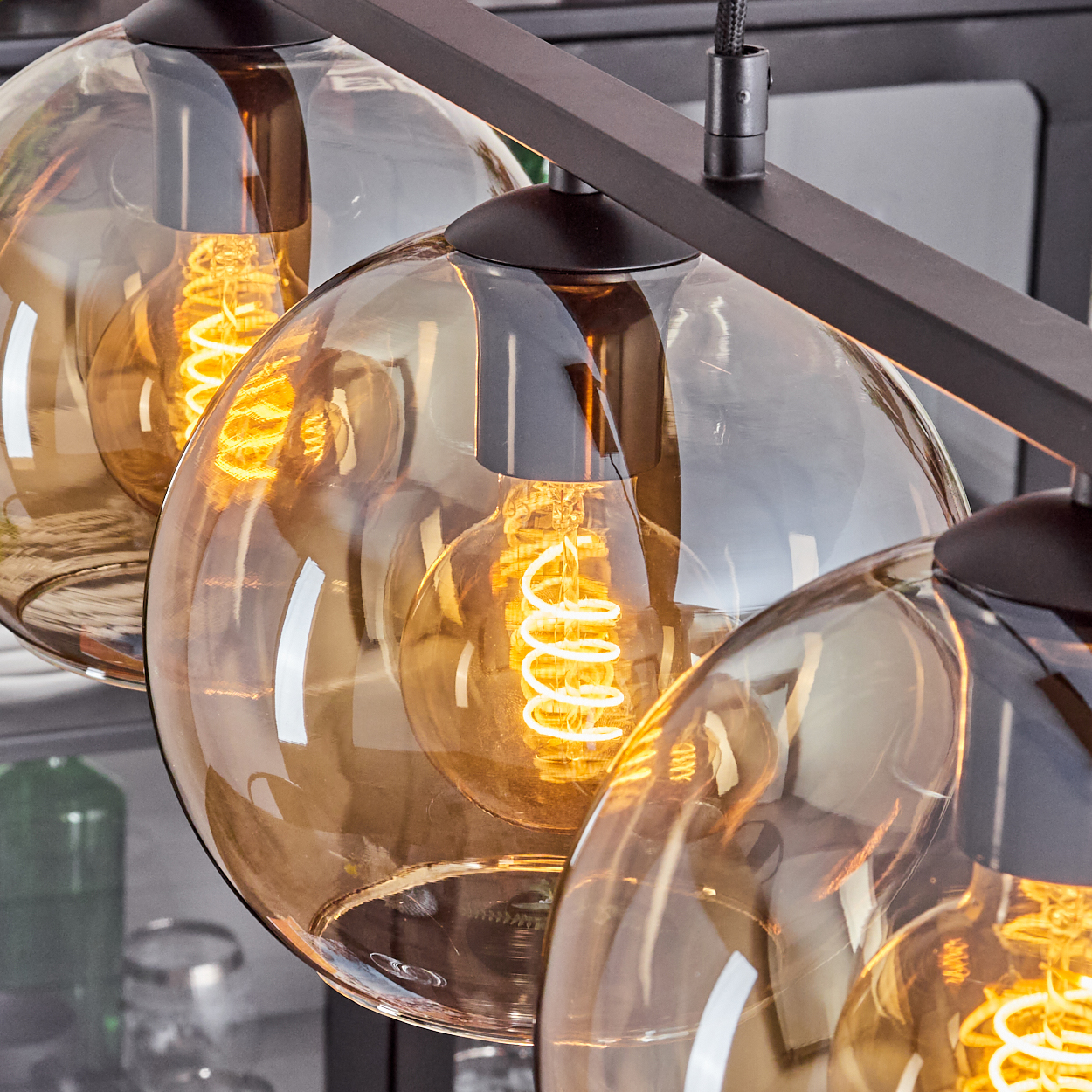 Nahaufnahme von drei Pendelleuchten mit bernsteinfarbenen Glasschirmen, Edison-Glühbirnen und schwarzer Tragstruktur.