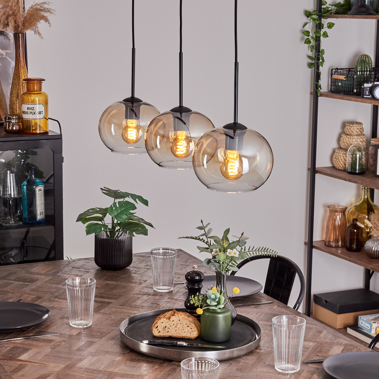 Drei bernsteinfarbene Glas-Hängeleuchten über einem Esstisch. Der Hintergrund umfasst einen schwarzen Tisch und Dekoration.