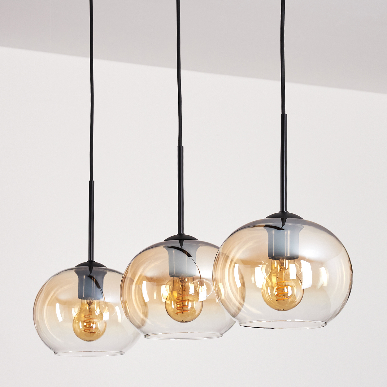 Drei Pendelleuchten mit bernsteinfarbenen Glasschirmen und Edison-Glühbirnen, schwarzen Kabeln, weiß.