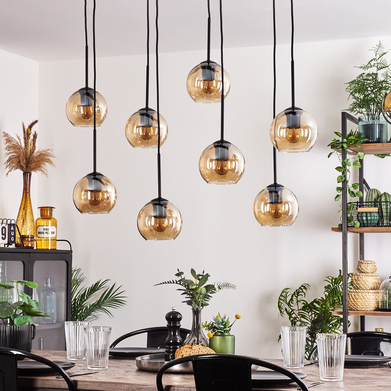 Esszimmer, acht hängende Glas-Pendelleuchten. Holztisch, Pflanzen und andere Dekorationen sind sichtbar.