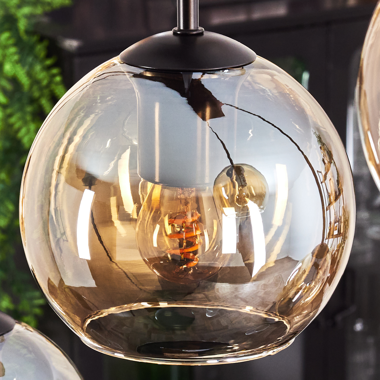 Nahaufnahme einer bernsteinfarbenen Pendelleuchte mit Edison-Glühbirne, zeigt Reflexionen und Details.