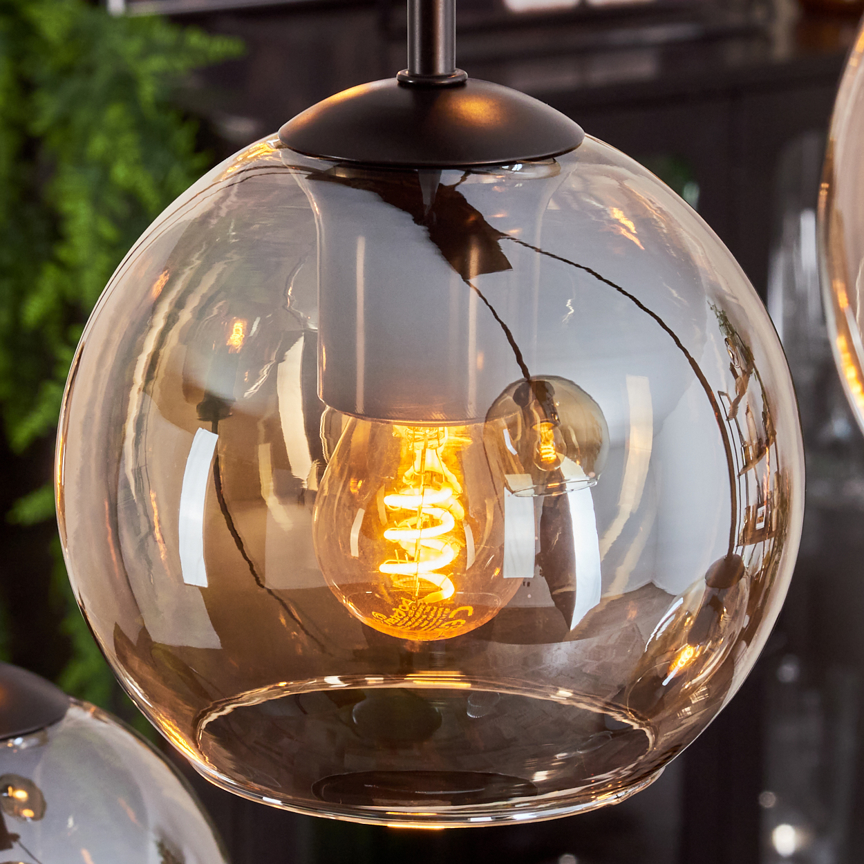 Nahaufnahme einer bernsteinfarbenen Pendelleuchte mit Edison-Glühbirne, zeigt Details und Reflexionen.