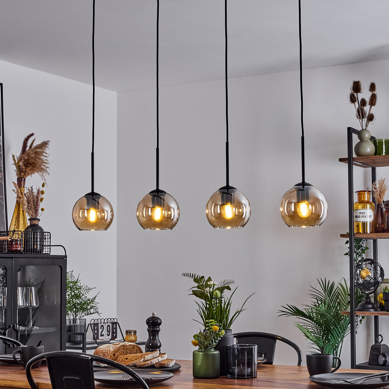Esszimmer mit vier Pendelleuchten mit bernsteinfarbenen Glaskugeln, über einem Holztisch. Pflanzen und Deko vorhanden.