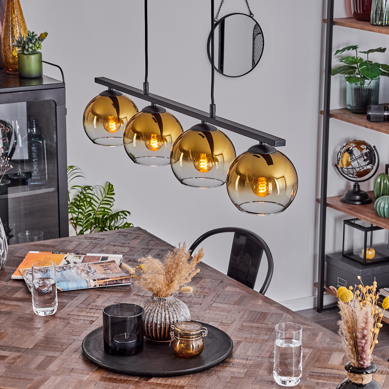 Esszimmer. Vier Pendelleuchten über einem Holztisch. Deko und Geschirr sind vorhanden.