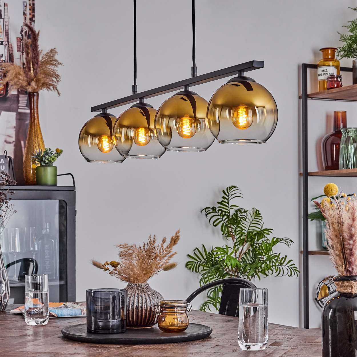 Esszimmer mit vier Pendelleuchten. Die Leuchten haben bernsteinfarbene Glasschirme. Ein Tisch ist mit Gläsern gedeckt.