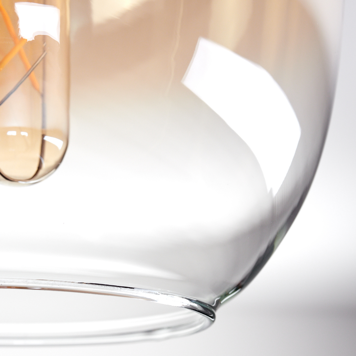 Nahaufnahme eines bernsteinfarbenen Glasschirms. Die Glühbirne ist innen sichtbar. Das Glas hat Reflexionen.